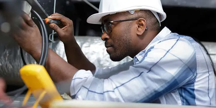 تاسیسات الکتریکی و سیم کشی برق ساختمان چیست؟ _ تصویری از فردی با کلاه ایمنی در حال بررسی تاسیسات الکتریکی