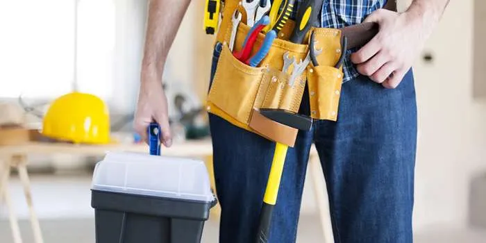 تصویری از دستها و بدن فردی که تعمیرکار ساختمانی است و لباس کار بر تن دارد.