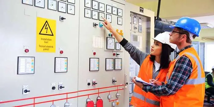 تاسیسات الکتریکی و سیم کشی برق ساختمان چیست؟ _ تصویری از زن و مردی که لباس کار بر تن دارند و در حال چک کردن تاسیسات الکتریکی ساختمان هستند.
