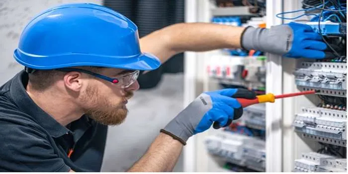 تصویری از یک فرد که با کلاه ایمنی آبی در حال کار کردن روی تاسیسات الکتریکی ساختمان است.